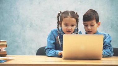 Cute little schoolkids sitting at the desk, involved in playing of computer game.