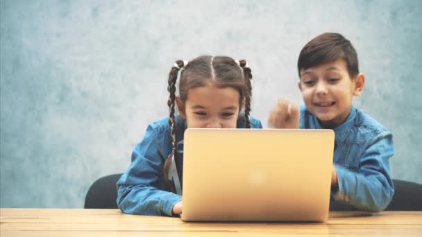 Petits écoliers mignons assis sur le bureau, impliqués dans le jeu d'ordinateur, gagner et lever joyeusement leurs mains, danser . — Video