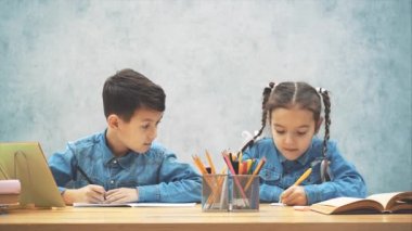 Okul çocukları ödevlerini yapıyor, erkek kardeşi kız kardeşini yazıyor. Kız kardeşi ona dikkat çekici bir şekilde bakıyor..