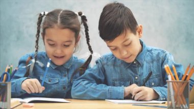 Schoolkids yazma, güzel küçük sisiter o ne yazdığını kardeşi gösteriyor, kardeşi başparmak kadar veriyor, ve kız kardeşi petting.