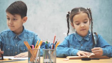 Meraklı küçük kız öğrenci yazıyor, sonra loupe aracılığıyla kameraya bakarak, gülümseyerek. Çocuk yazıyor..