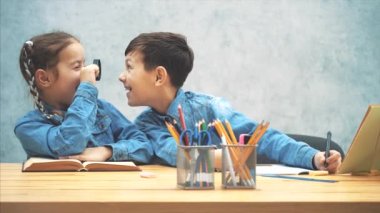 Meraklı küçük kız öğrenci bir loupe ile kardeşi muayene, gülümseyerek. Etrafta oynuyorlar, gaddarlık yapıyorlar..