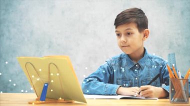 Genç konsantre okul çocuğu mavi kot pantolon t-shirt yazma, kitap sahibi üzerinde kitaptan metin kopyalama. Kız kardeşi ona katılıyor, nasıl yazdığına bakıyor. Onu savuşturuyor..