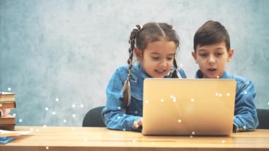 Cute little schoolkids sitting at the desk, involved in playing of computer game.