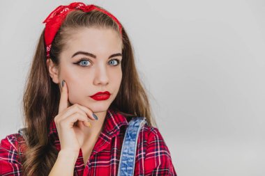 Beautiful young girl in red standing, holding hands near her chin, posing, looking at the camera thoughtfully.