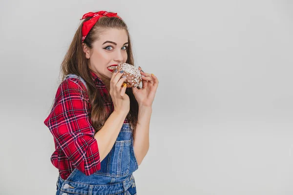 Neugierige junge Frau isst großen Schokokrapfen und schleicht, als ob sie sich vor jemandem versteckt. — Stockfoto