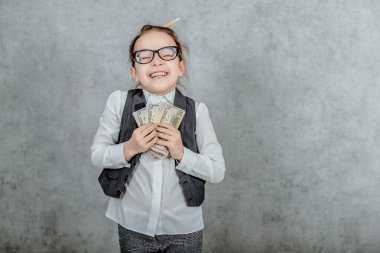 Genç bir iş kadınının yakın çekimi gri bir arka planda duruyor. Bu süre zarfında, parayı elinde tutuyor. Gözlük takmış. Gülümseyin..