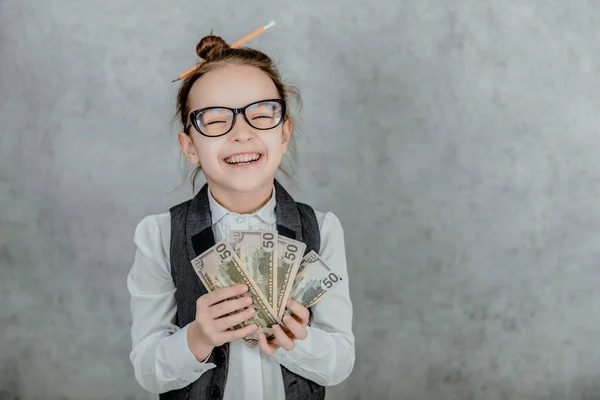 若いビジネスの女性のクローズアップは灰色の背景に立っています。この間、それはお金を手元に置きます。眼鏡に身を包んだ笑顔 — ストック写真