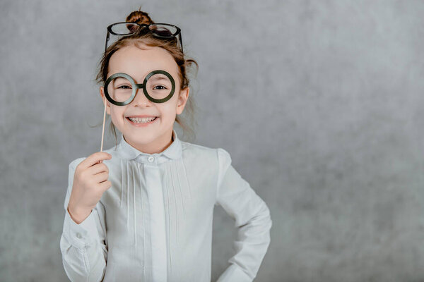 Little business girl on a gray background. During this time, holds cardboard black glasses.