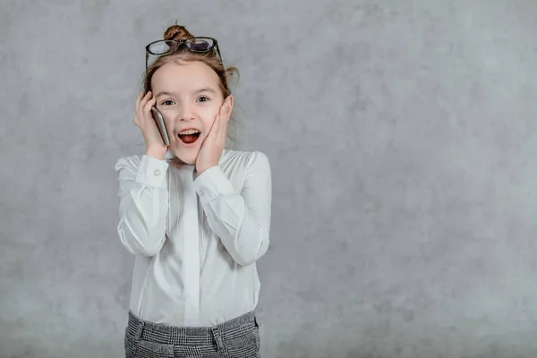 Bilden av känslomässigt glada ansikten. En liten skolflicka. Le och prata med en smart telefon och visa handen för att hålla kampen tecken. Begreppet affärskommunikation — Stockfoto