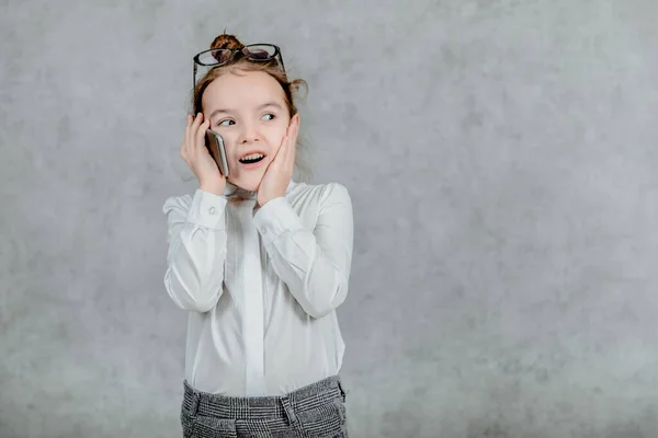 Bilden av känslomässigt glada ansikten. En liten skolflicka. Le och prata med en smart telefon och visa handen för att hålla kampen tecken. Begreppet affärskommunikation — Stockfoto