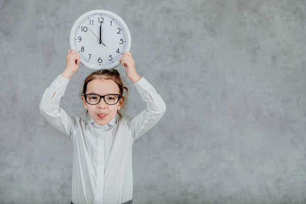 Hermosa niña con un reloj sobre un fondo gris. Levanta las manos con el reloj. Emocional —  Fotos de Stock