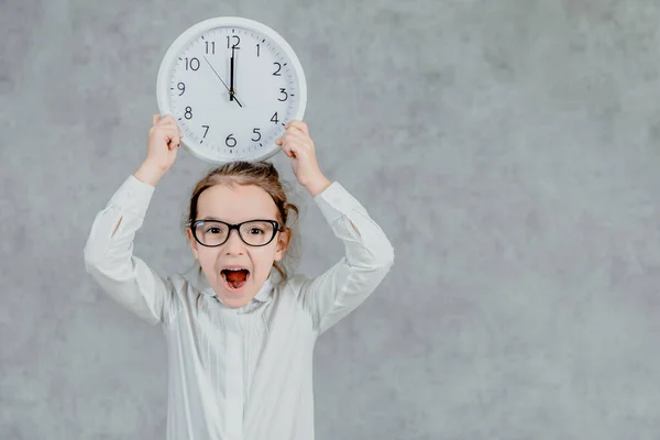 Hermosa niña con un reloj sobre un fondo gris. Levanta las manos con el reloj. Emocional —  Fotos de Stock