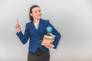 Bir yığın renkli kitap tutan mutlu bayan öğretmen, parmağını kaldırıyor, bir şeye dikkat etmek için arıyor, gülümsüyor..