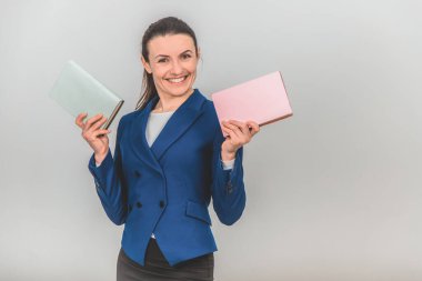 Elinde iki renkli kitap tutan, poz veren ve gülümseyen sevimli bayan öğretmen..