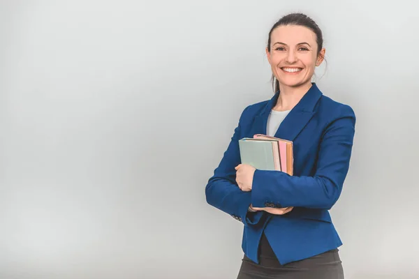 Preciosa maestra sosteniendo una pila de libros coloridos cerca de su pecho, mirando a la cámara, sonriendo . — Foto de Stock