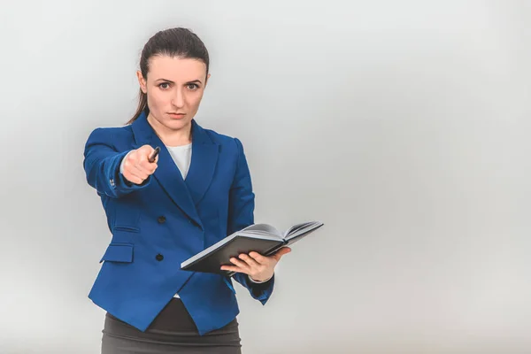 Strict teacher standing with notebook her hands, pointing pen at the camera as if calling someone to go to the blackboard. — Stock Photo, Image