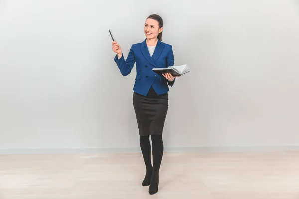 Full-length teacher standing with notebook opened and pointing her hand with pen up, calling to pay attention to what she is talking about. — Stock Photo, Image