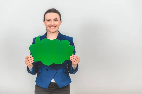 Female teacher standing, holding a green cloud-shape speech bubble, looking at the camera, smiling.