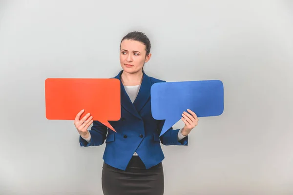 Young female teacher holding two speech bubbles, looking at them with confused face expression. — Stock Photo, Image