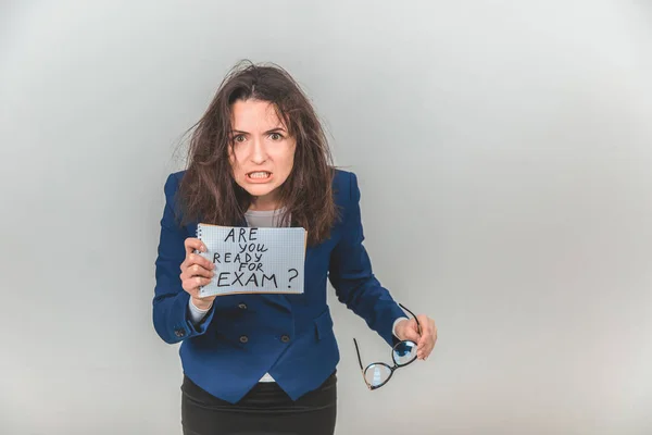 Totalement fatigué jeune enseignant est debout, tenant une feuille de papier avec prêt pour l'examen écrit sur elle. Ses cheveux sont ébouriffés, elle met ses dents, elle a l'air folle . — Photo