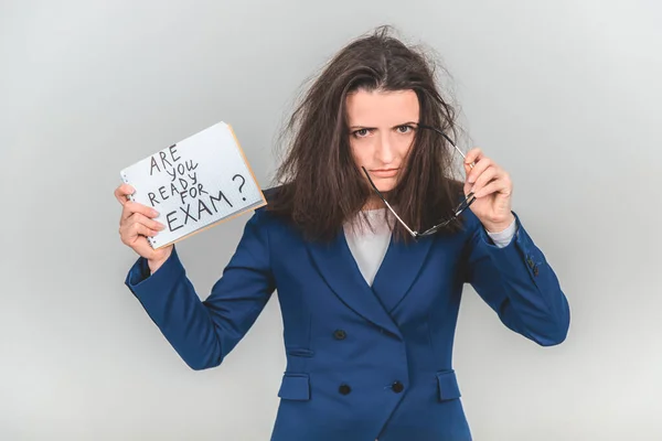 Totalement fatigué jeune enseignant est debout, tenant une feuille de papier avec prêt pour l'examen écrit sur elle. Ses cheveux sont ébouriffés, elle regarde la caméra comme si elle détestait tout le monde . — Photo