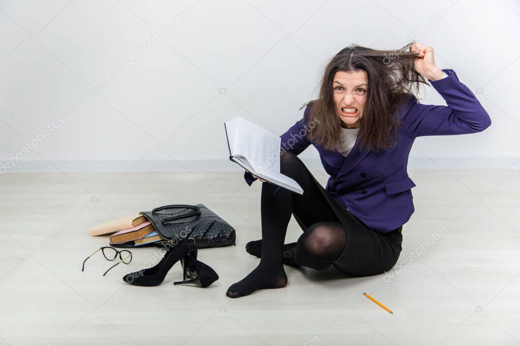 Insane young teacher with tousled hair, setting her teeth, tearing out her hair, sitting on the floor.