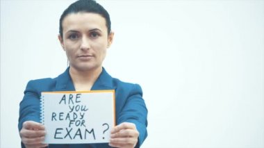 Ciddi bir öğretmen beyaz bir arkaplanda duruyor. Sayfaya yazılan kelimeleri tutun. Sınava hazır mısınız? Gözlük takmış..