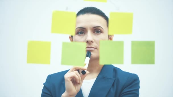 Un hombre de negocios escribe notas de pegamento en una pared de vidrio en el lugar de trabajo. Adhesivo recordatorio de papel calendario para discutir la idea creativa. Lluvia de ideas de negocios . — Vídeos de Stock