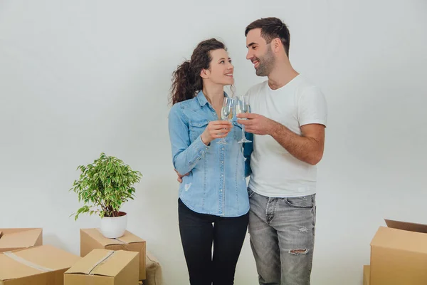 Shot of charming copule standing with glasses of champange, celebrating their move into new apartment, smiling, looking at one another with love in eyes. — Stock Photo, Image