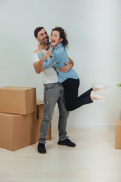 Couple moving into their new house. Woman is very glad and is hanging on her husbands neck, hugging him. — Stock Photo, Image