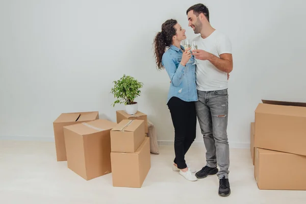 Shot of charming copule standing with glasses of champange, celebrating their move into new apartment, hugging, smiling, looking at one another with love in eyes. — Stock Photo, Image