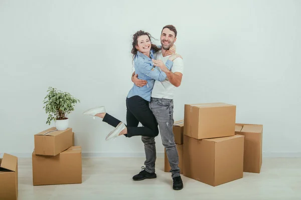 Um casal a mudar-se para a sua nova casa. Mulher é muito feliz e está pendurado em seu pescoço maridos, abraçando-o . — Fotografia de Stock