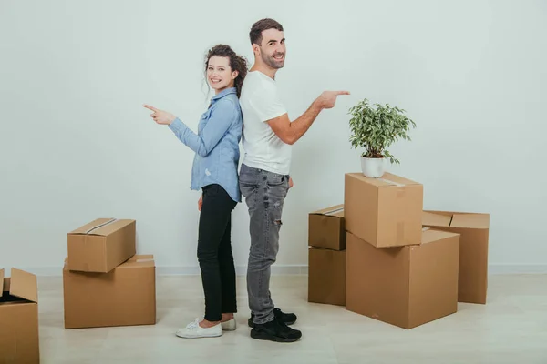 Happy wife and husband standing back to back, smiling pointing their fingers to the sides at the copy space. — Stock Photo, Image