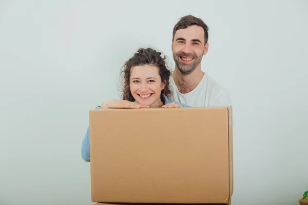 Esposa sonriente y marido de pie detrás de la caja de cartón grande, juntos, abrazándose, mirando a la cámara . — Foto de Stock