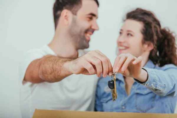 Joyfull wife and husband standing behind the big carton box, , holding together in front of the camera keys to their new flat . — Stock Photo, Image