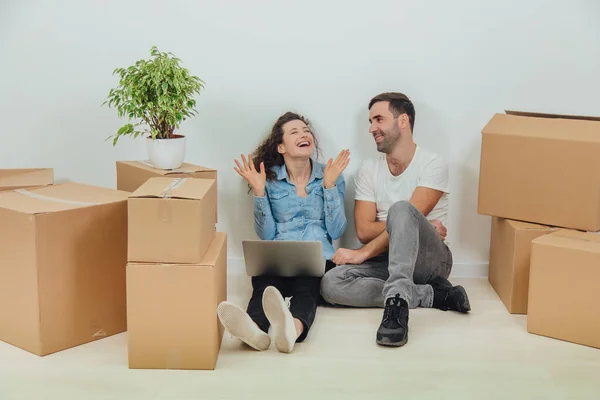 Young couple with laptop in the apartment, sitting on the floor, surfing in the internet, looking for new furniture. Woman is exstremely happy. — Stock Photo, Image