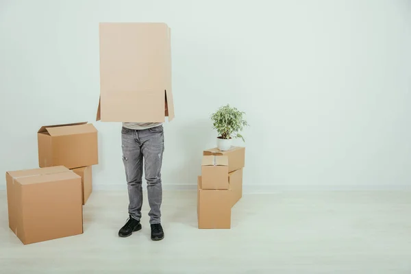 O homem engraçado está de pé com uma caixa de papelão na cabeça. Jovem bonito movendo-se para a casa nova . — Fotografia de Stock