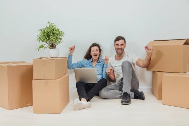 Dairede dizüstü bilgisayarı olan genç bir çift, yerde oturuyor, internette sörf yapıyor, ellerini kaldırıyor, 