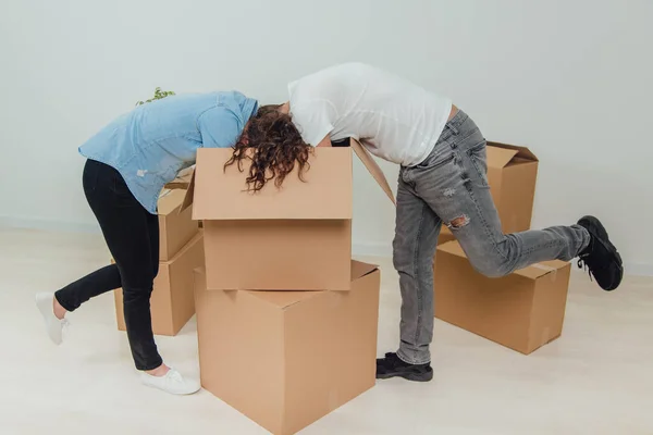 Esposa e marido estão ocupados, desempacotando as caixas de papelão. Eles estão de pé abaixando suas cabeças na caixa grande . — Fotografia de Stock