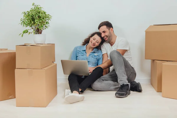 Young couple with laptop in the apartment, sitting on the floor, surfing in the internet, looking for new furniture. — Stock Photo, Image