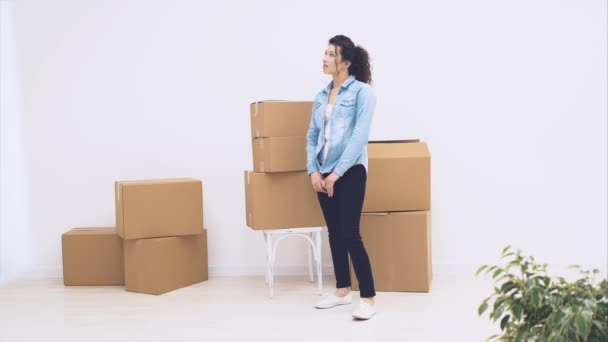 Young lady is standing near boxes and is thinking from what to start. She is looking around. 4K. — Stock Video