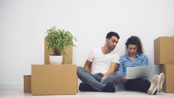 Pareja joven se muda a un nuevo apartamento juntos. Ellos están pensando de qué empezar, mirando a la pantalla del ordenador portátil. Acción. Animación. 4K . — Vídeo de stock