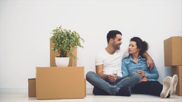 La feliz pareja está hablando mientras está sentada en el suelo y sosteniendo vasos de vino blanco. Acción. 4K . — Vídeos de Stock