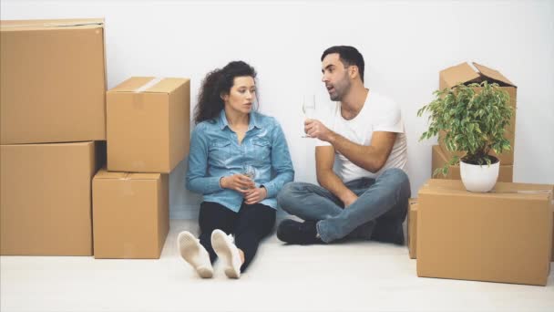 La feliz pareja está hablando mientras está sentada en el suelo y sosteniendo vasos de vino blanco. Acción. 4K . — Vídeos de Stock