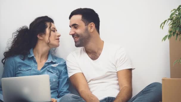 Pareja joven se muda a un nuevo apartamento juntos. Están sentados frente a la laptop. La pareja se besa y se abraza. De cerca. Acción. Animación. 4K . — Vídeo de stock