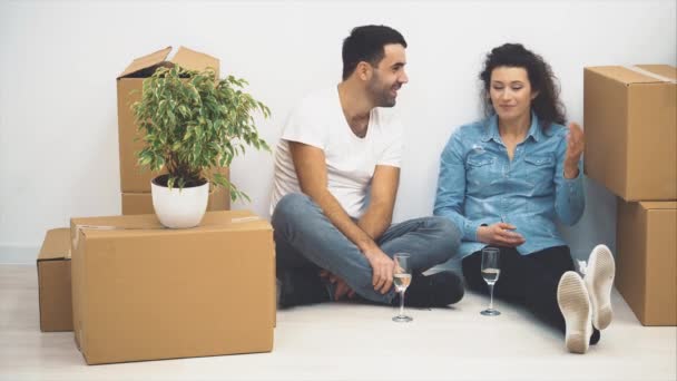 La feliz pareja está hablando mientras está sentada en el suelo y sosteniendo vasos de vino blanco. Acción. 4K . — Vídeos de Stock