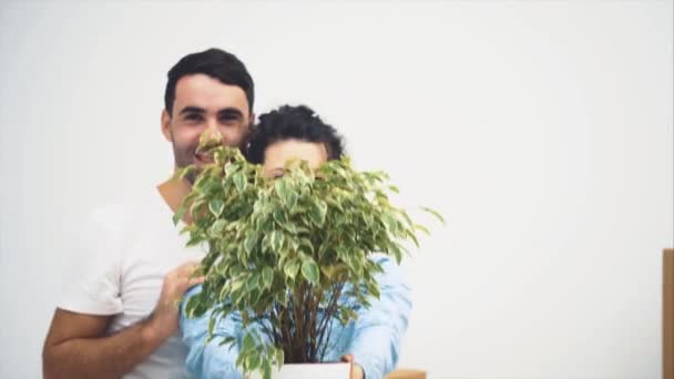 A fiatal pár együtt költözött egy új lakásba. Egy zöld virágcserepet tartanak és mosolyognak. Felvétel, animáció. 4k. — Stock videók