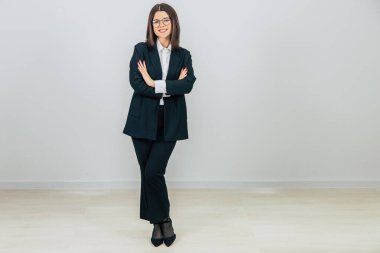 Siyah takım elbiseli genç, kendine güvenen bir iş kadını elleri bağlanmış, kameraya bakıyor, içtenlikle gülümsüyor..