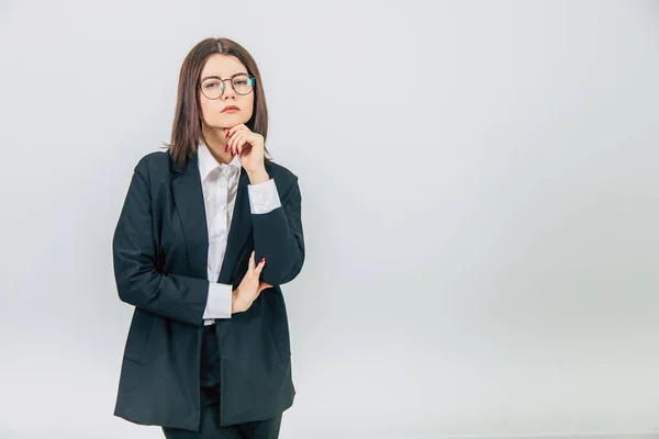 Attractive serious businesswoman in black suit standing, keeping hand on the chin, thinking, at the camera, narrowing her eyes. — Stock Photo, Image